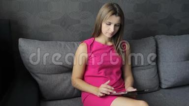 穿裙子的女人坐在沙发上用平板电脑。 坐在沙发上用平板电脑工作的女孩